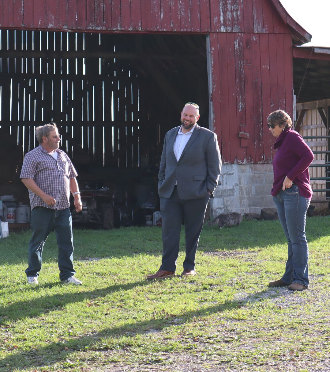Two farmers and someone from MSU Extension in front of a barn.